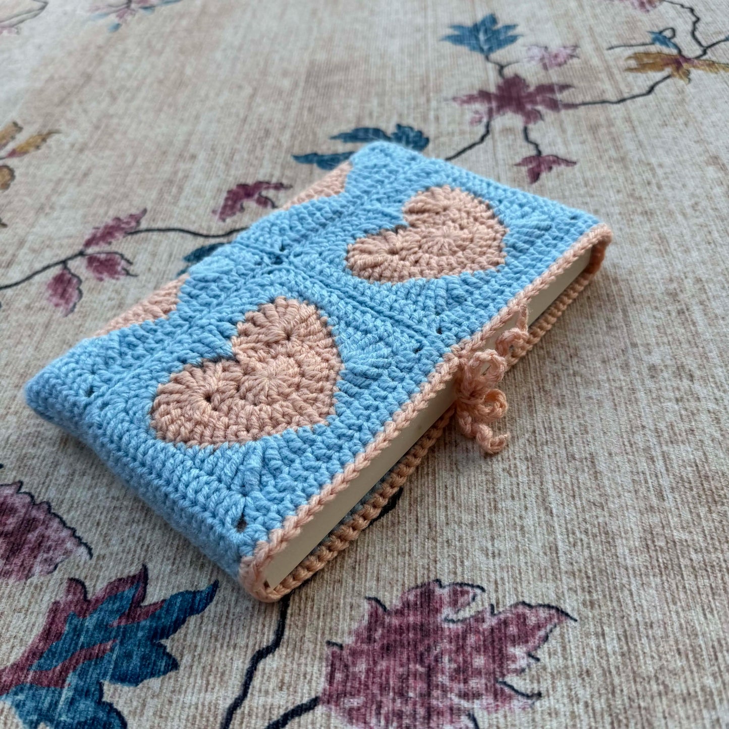 Crocheted book cover with heart patterns on a floral fabric background