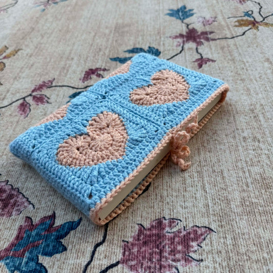 Crocheted book cover with heart patterns on a floral fabric background