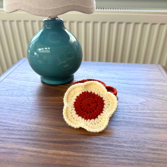 Crocheted coaster on a wooden surface with a teal lamp in the background