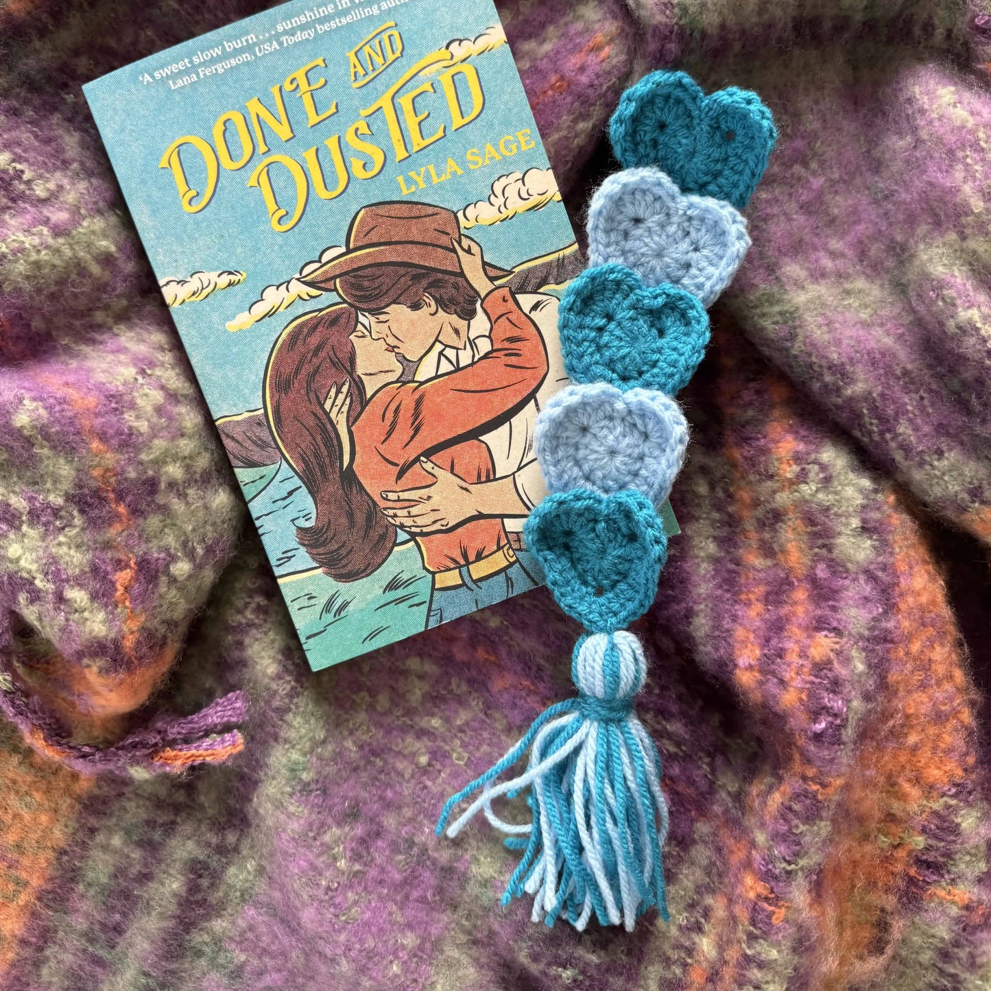 A blue and grey crecheted bookmark on a textured fabric background.