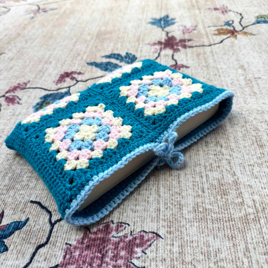 Crocheted blue cover with floral patterns on a book, placed on a floral fabric background