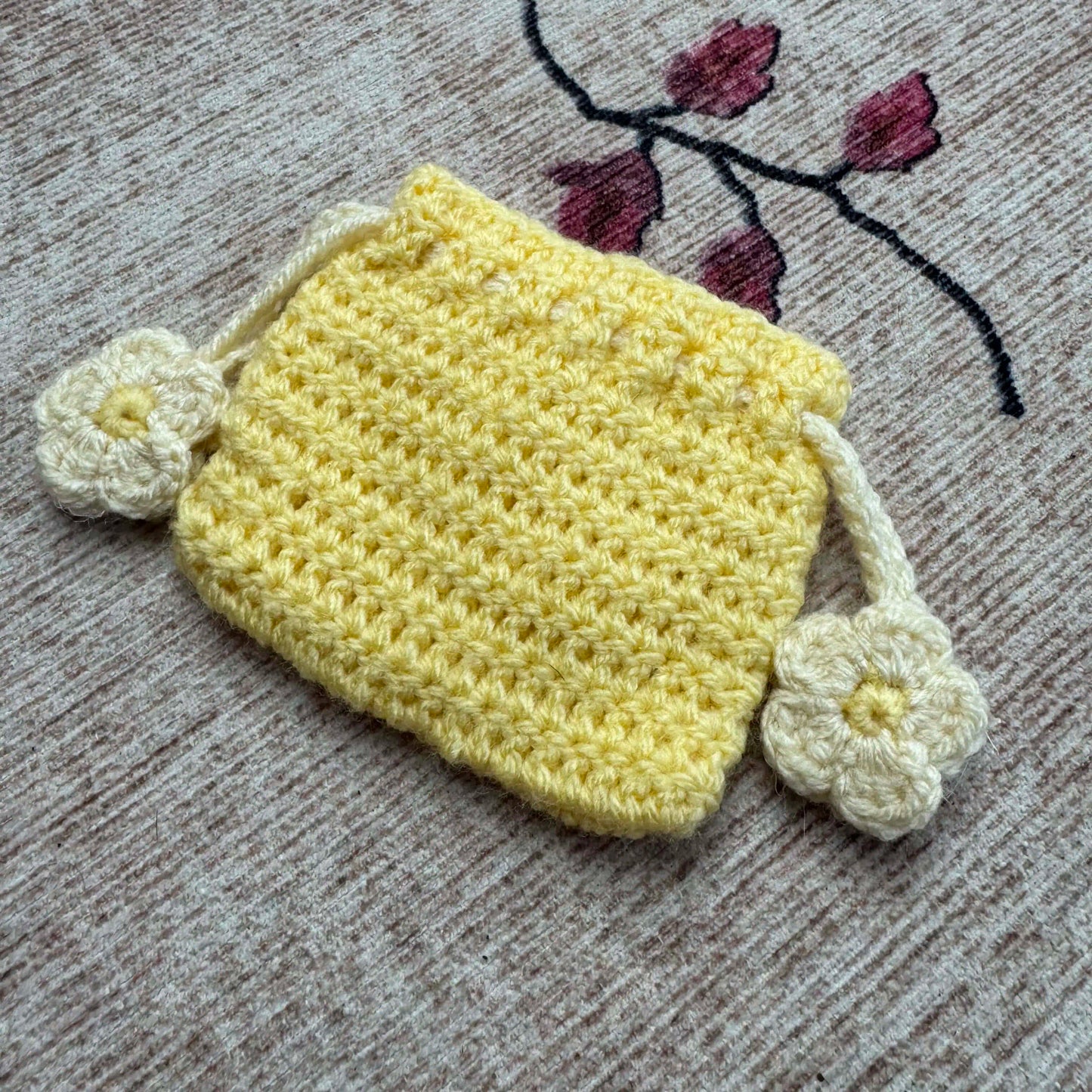 Yellow crocheted pouch with white flowers on a textured surface