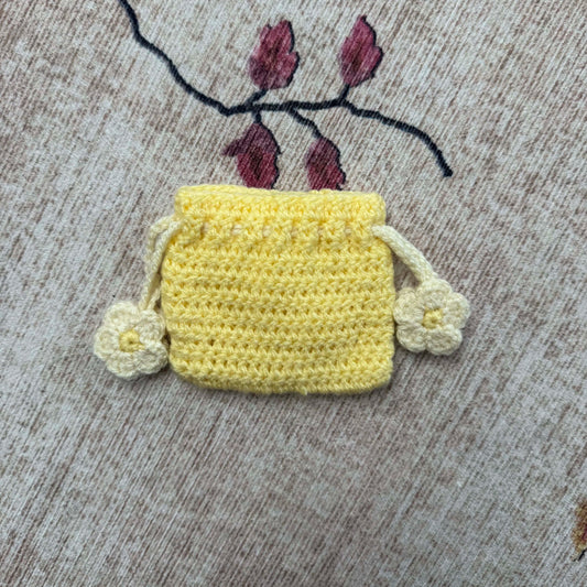 Crocheted yellow pouch with floral details on a textured fabric background