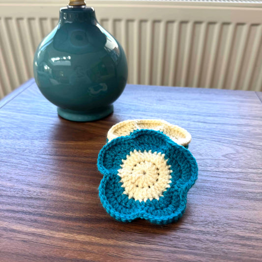 Crocheted coasters on a wooden surface with a teal ceramic vase in the background.