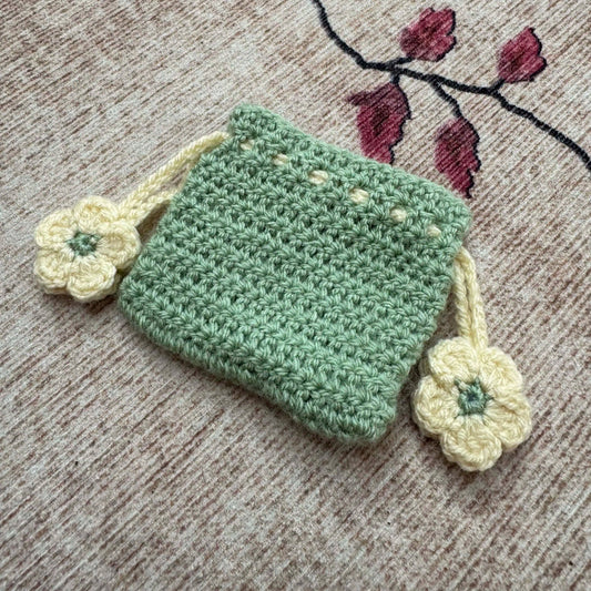 Green crocheted pouch with white flowers on a textured surface