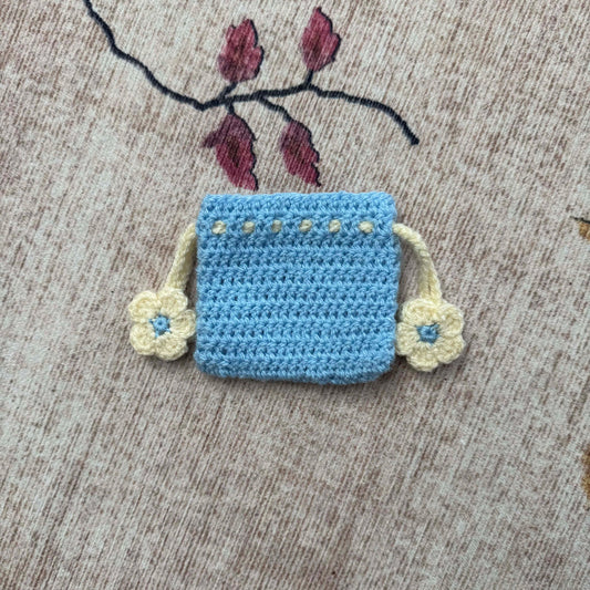 Crocheted blue pouch with floral details on a textured surface