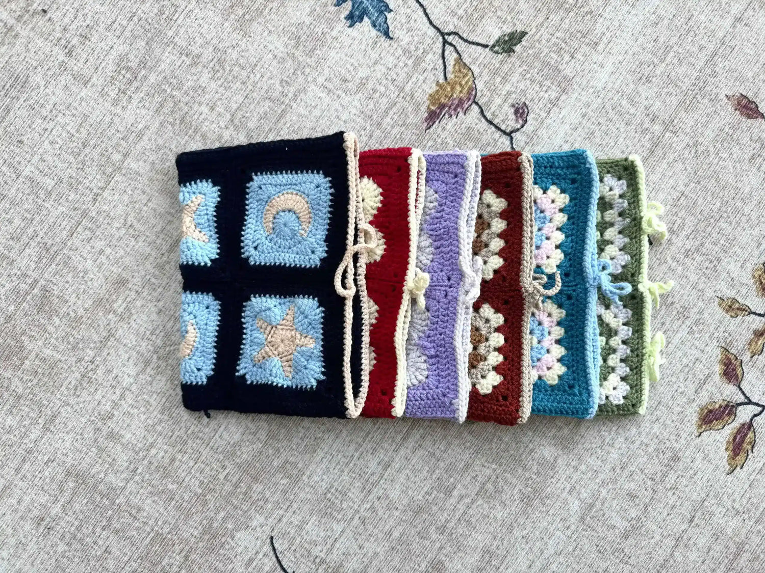 Stack of colourful crochet book covers on a textured fabric background.