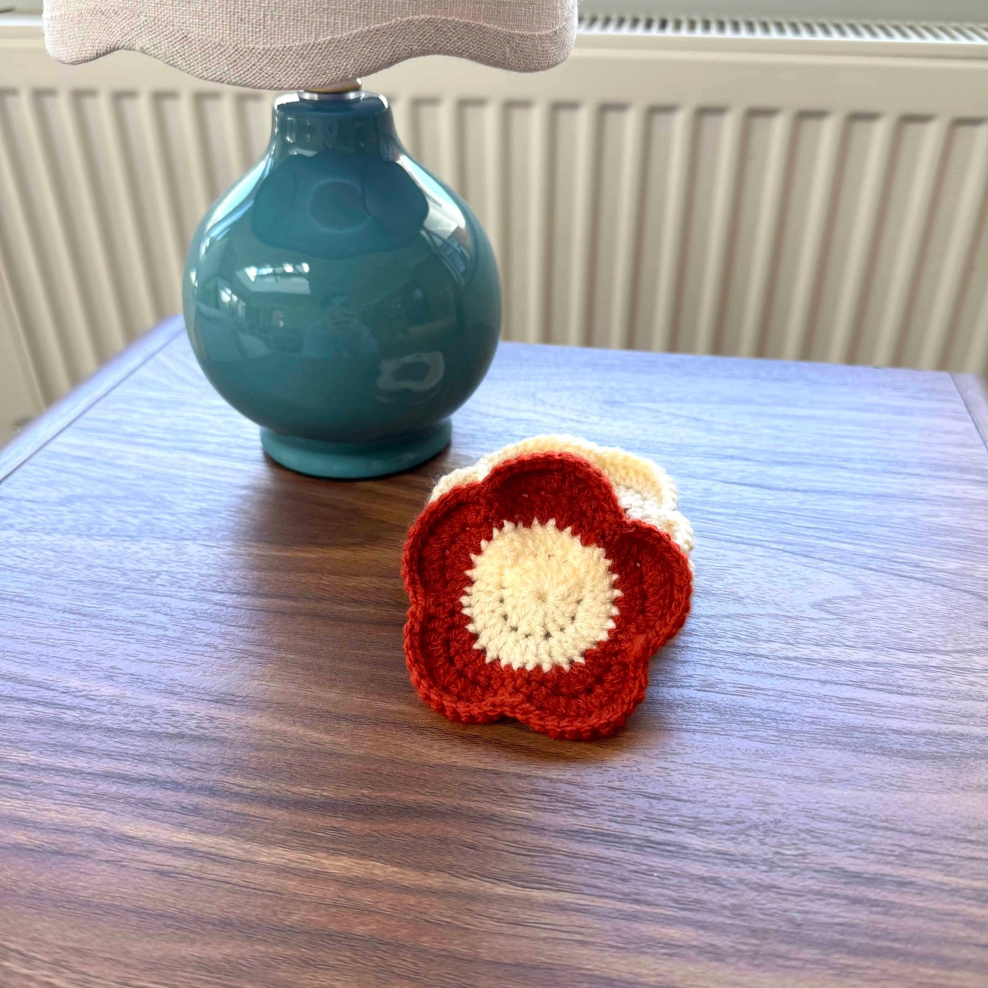 Crocheted coaster on a wooden table with a teal lamp in the background