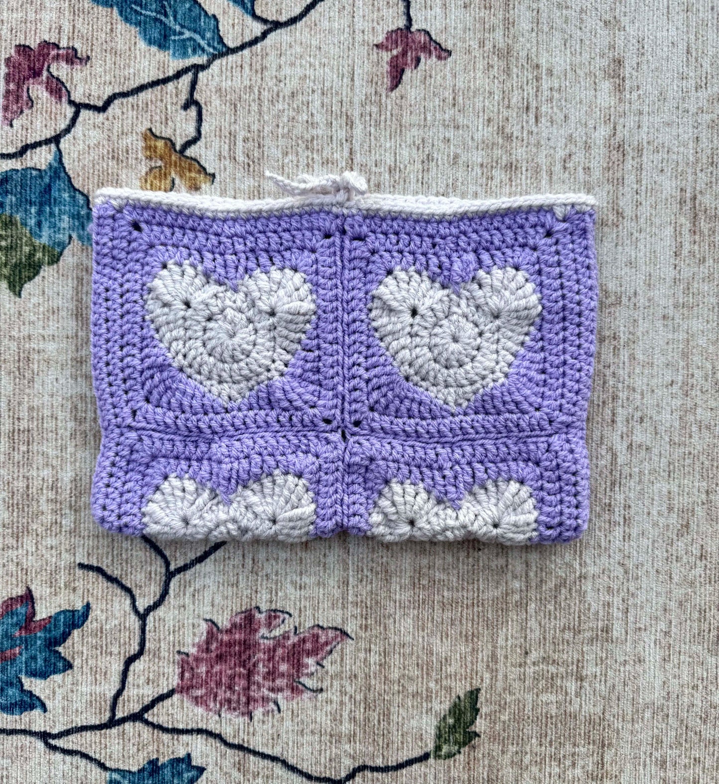Crocheted book cover with heart patterns on a textured fabric background