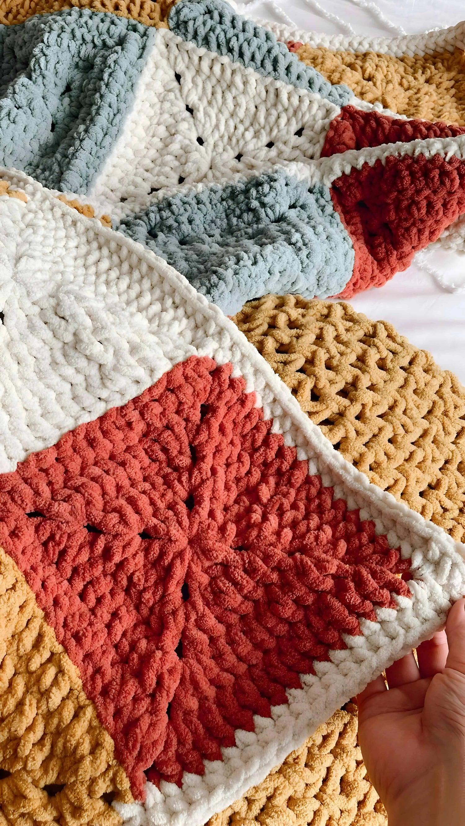 Colourful crocheted blanket with a patchwork pattern held by a hand.