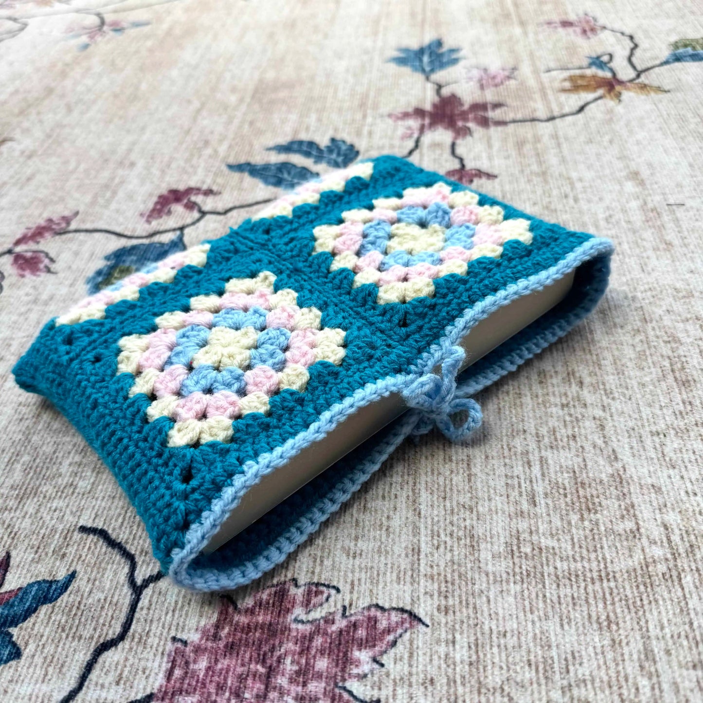 Crocheted blue cover with floral patterns on a book, placed on a floral fabric background