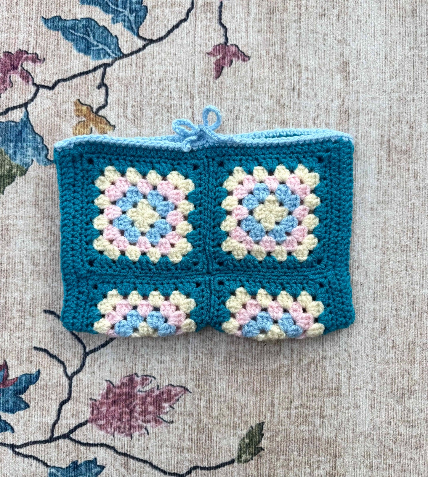 Crocheted book cover with blue border on a floral fabric background