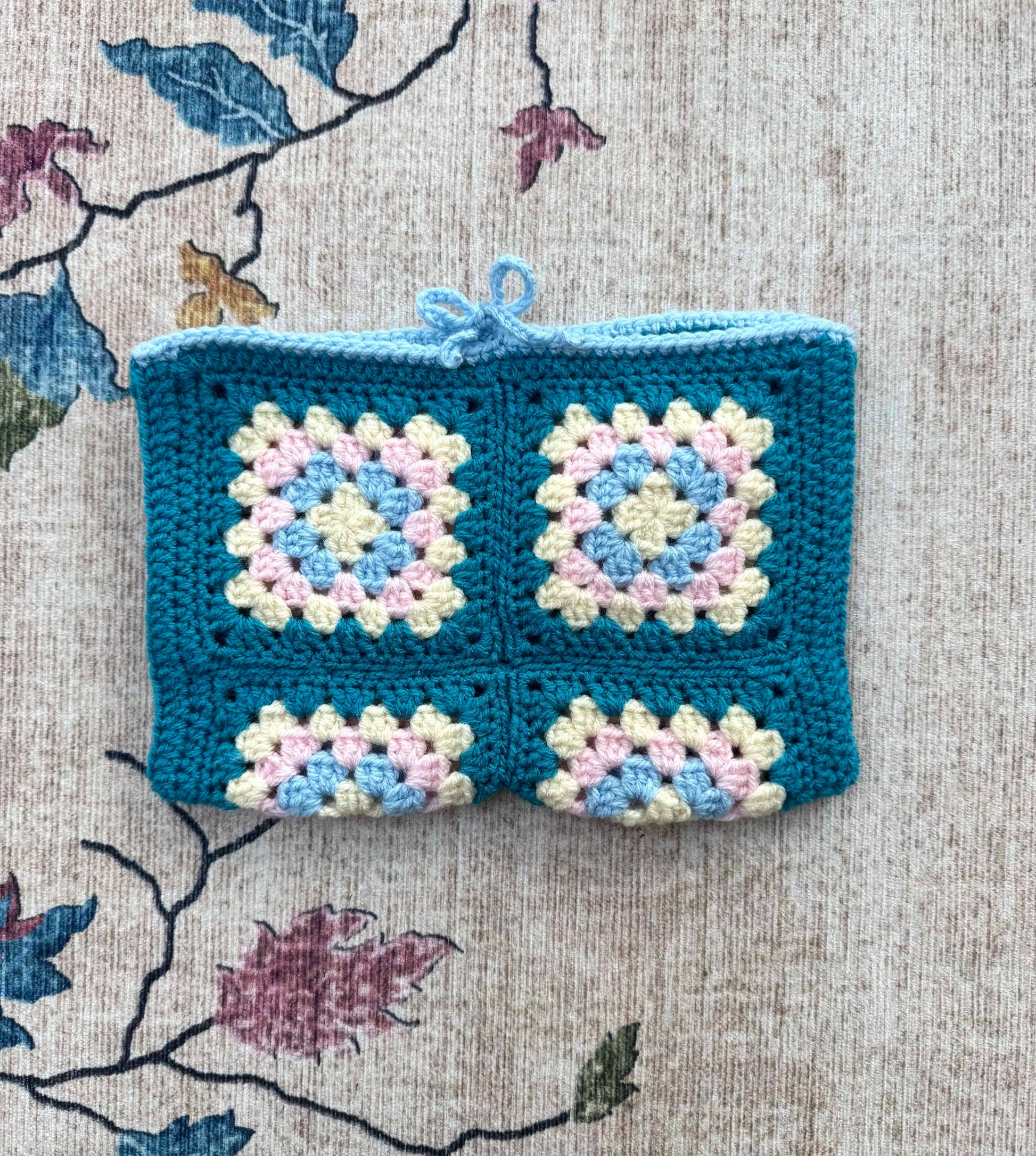 Crocheted book cover with blue border on a floral fabric background