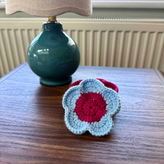 Crocheted coaster on a wooden surface with a green lamp in the background