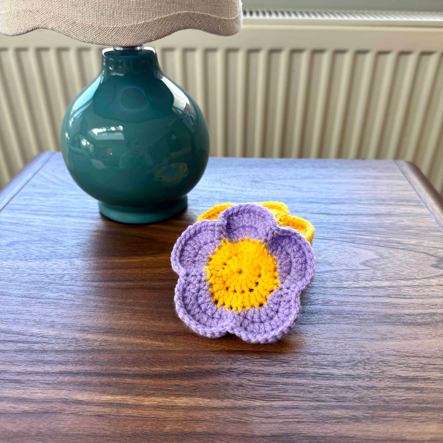 Crocheted flower coasters on a wooden surface with a teal lamp in the background.