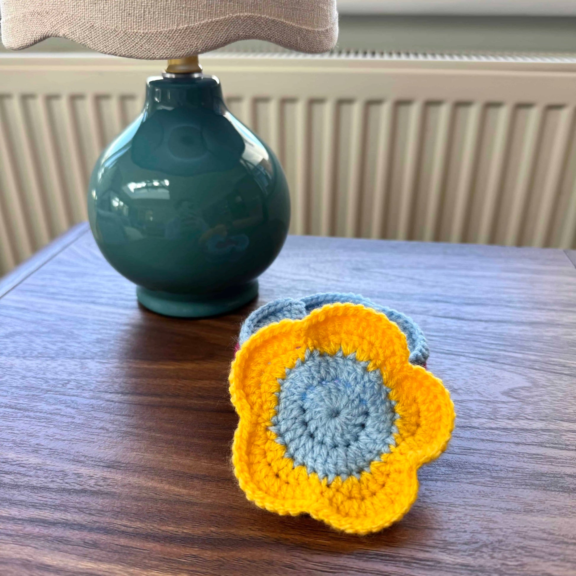Crocheted flower coasters on a wooden surface with a teal lamp in the background.