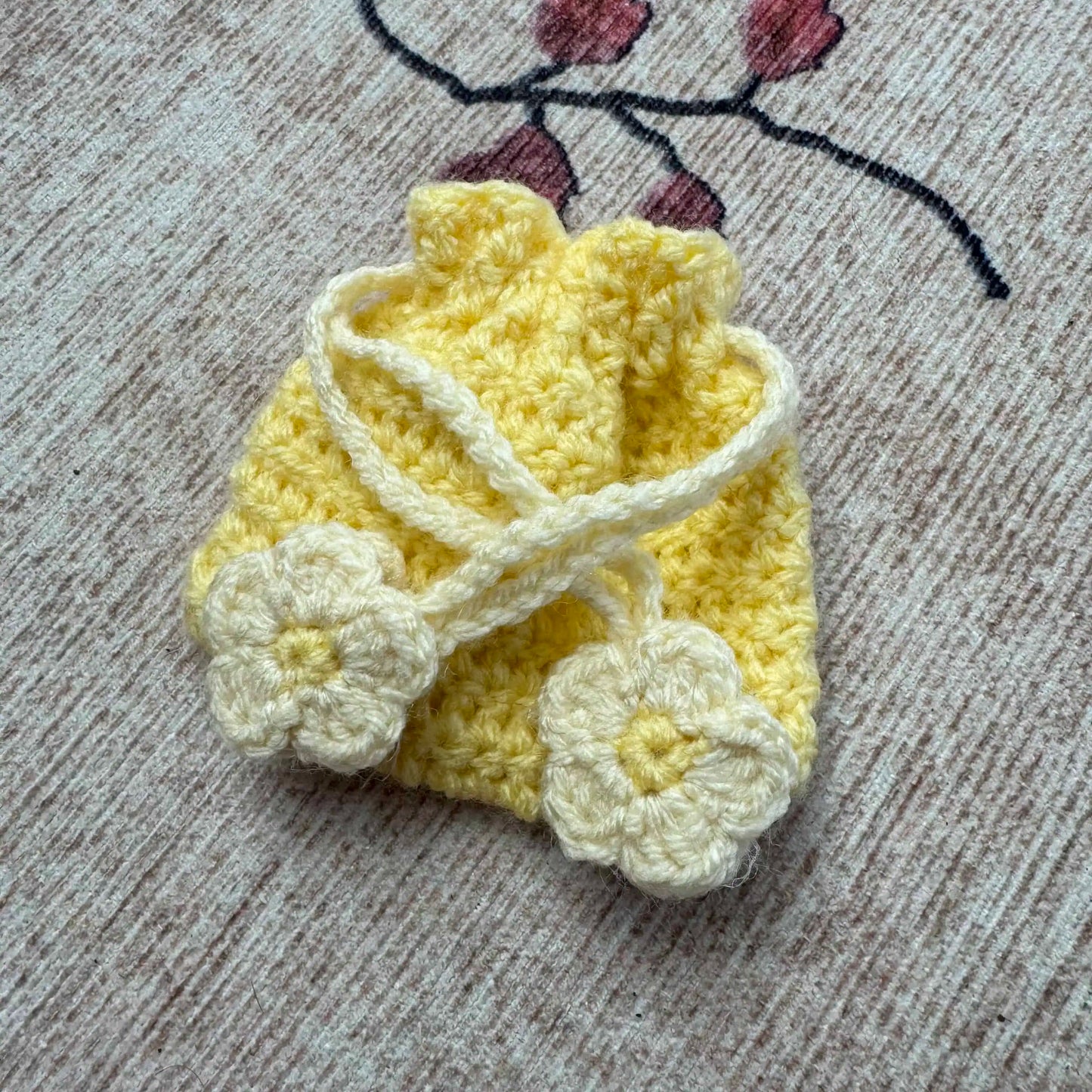 Yellow crochet pouch with white flowers on a textured surface