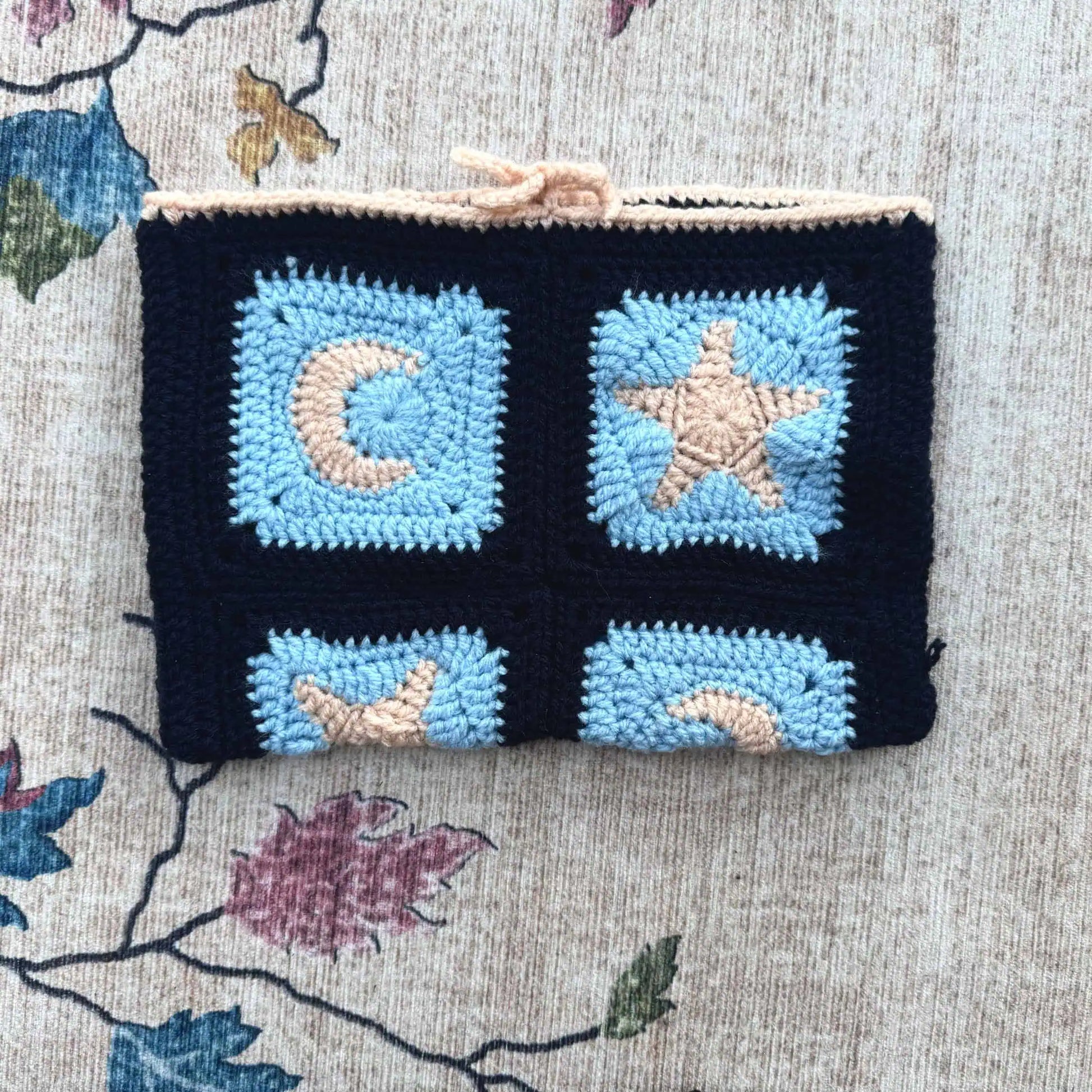 Crocheted book cover with star and moon designs on a floral fabric background