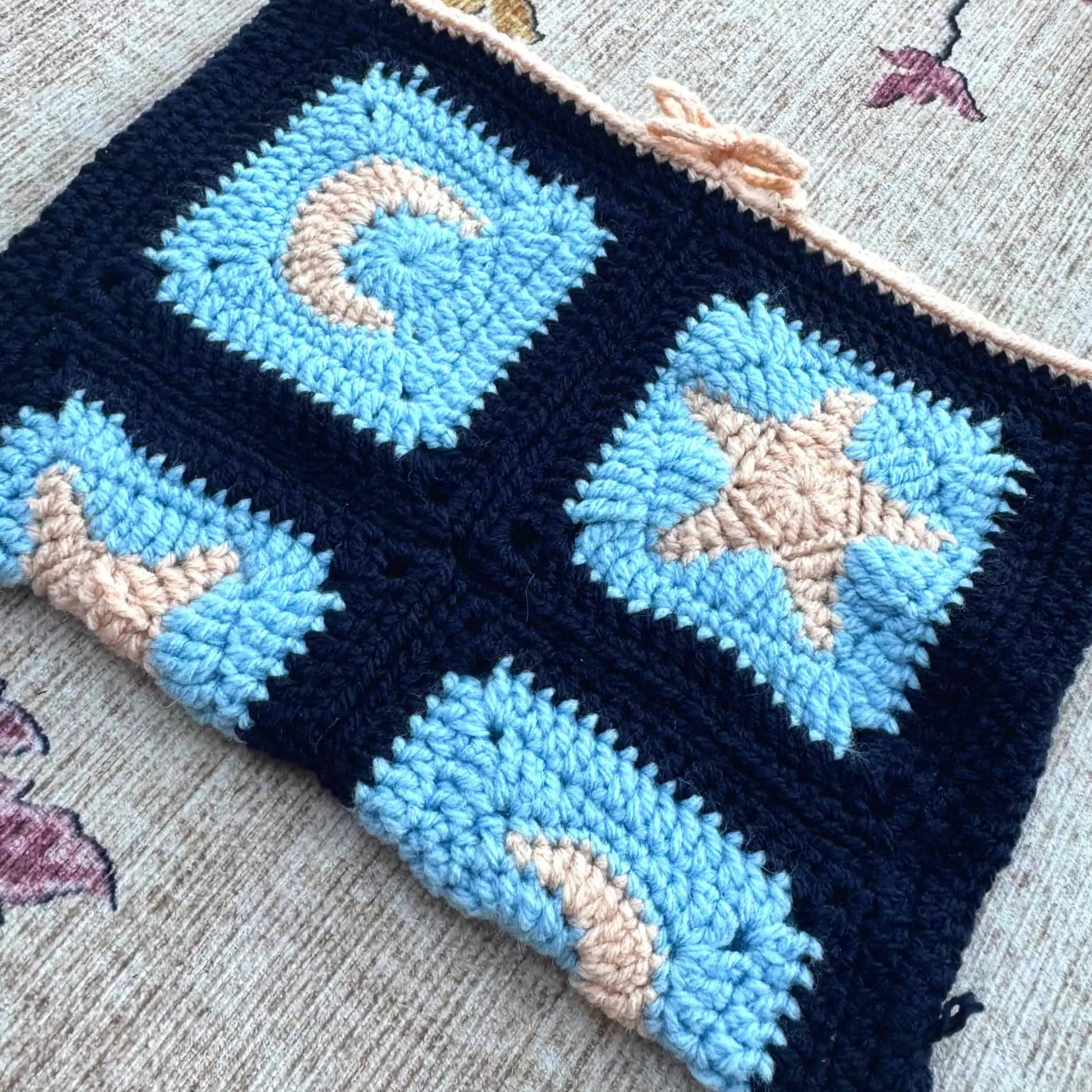 Crocheted book cover with blue and beige star and moon patterns.