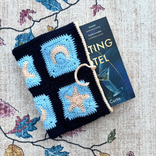 Crocheted blue and black book cover with star and moon design next to a book