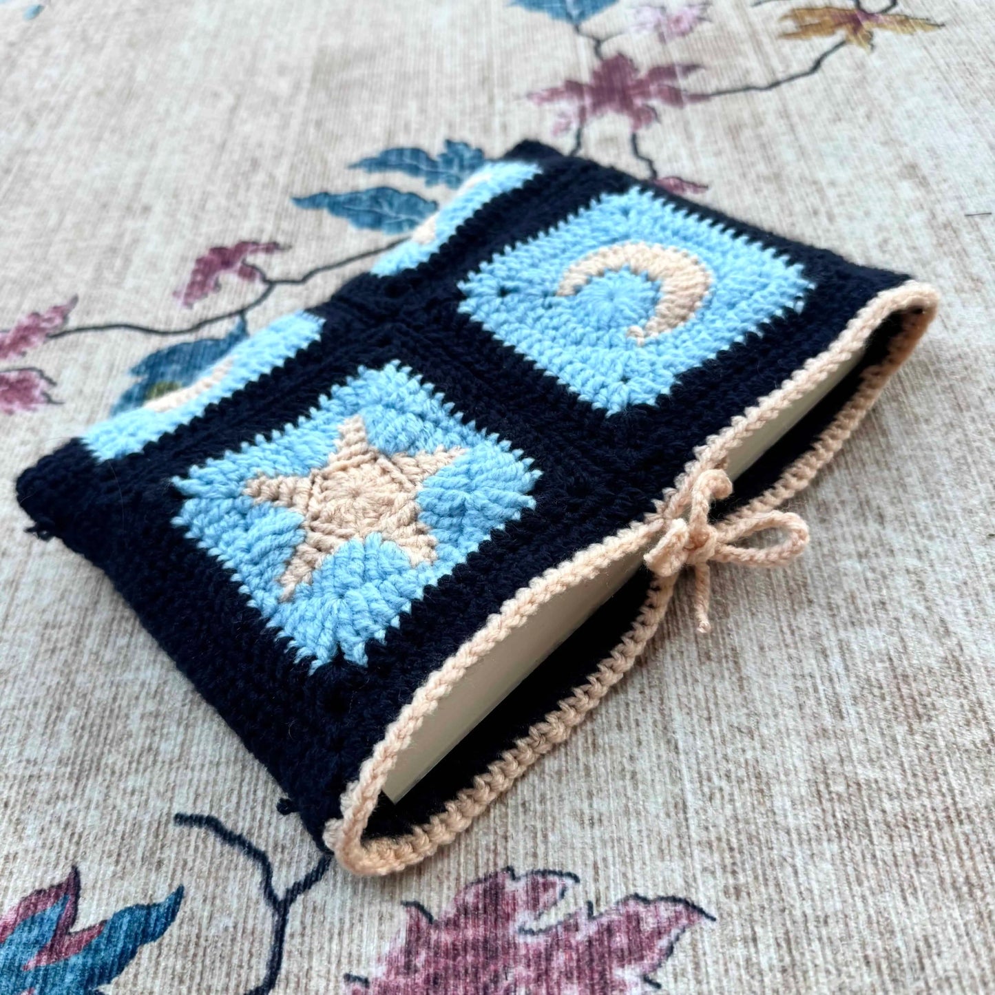 Crocheted book cover with star and moon patterns on a floral fabric background