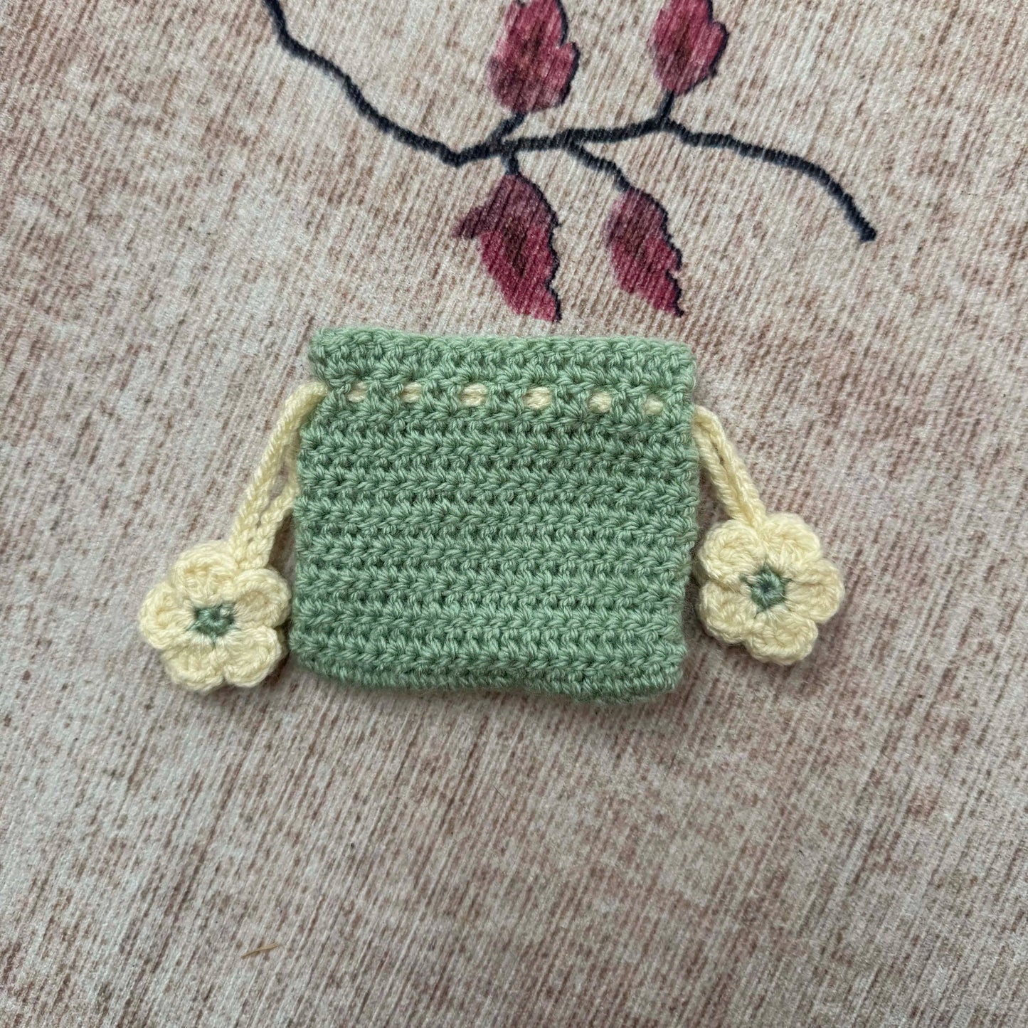 Small green crocheted bag with floral details on a textured surface