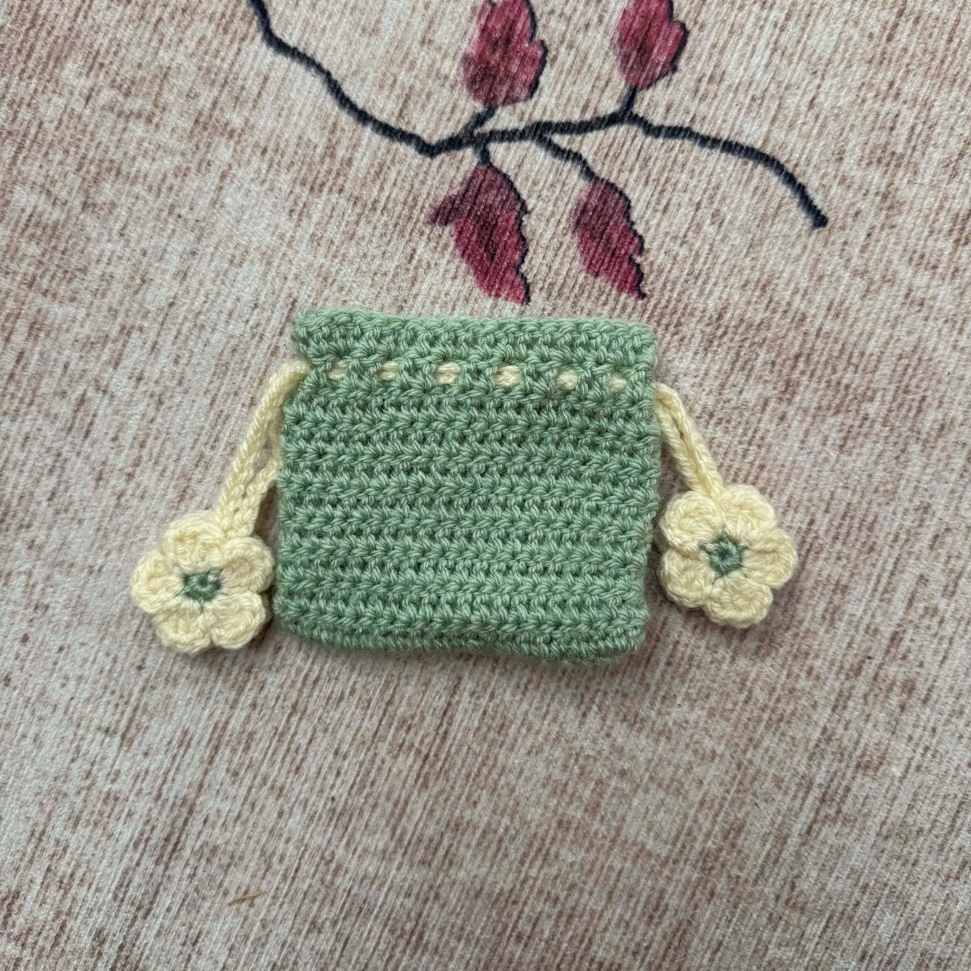 Small green crocheted bag with floral details on a textured surface