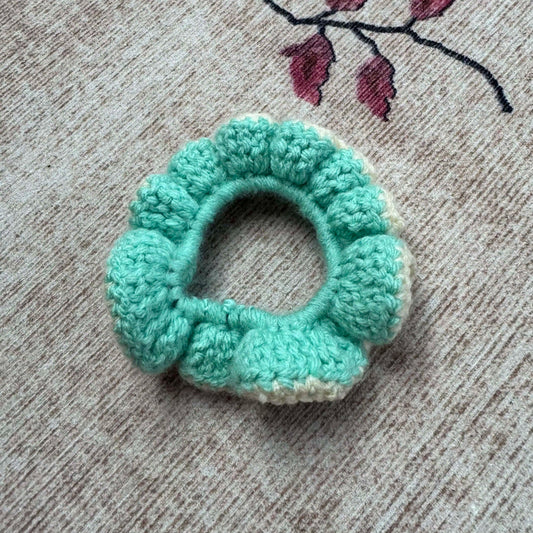 Turquoise crochet scrunchie on a textured surface.