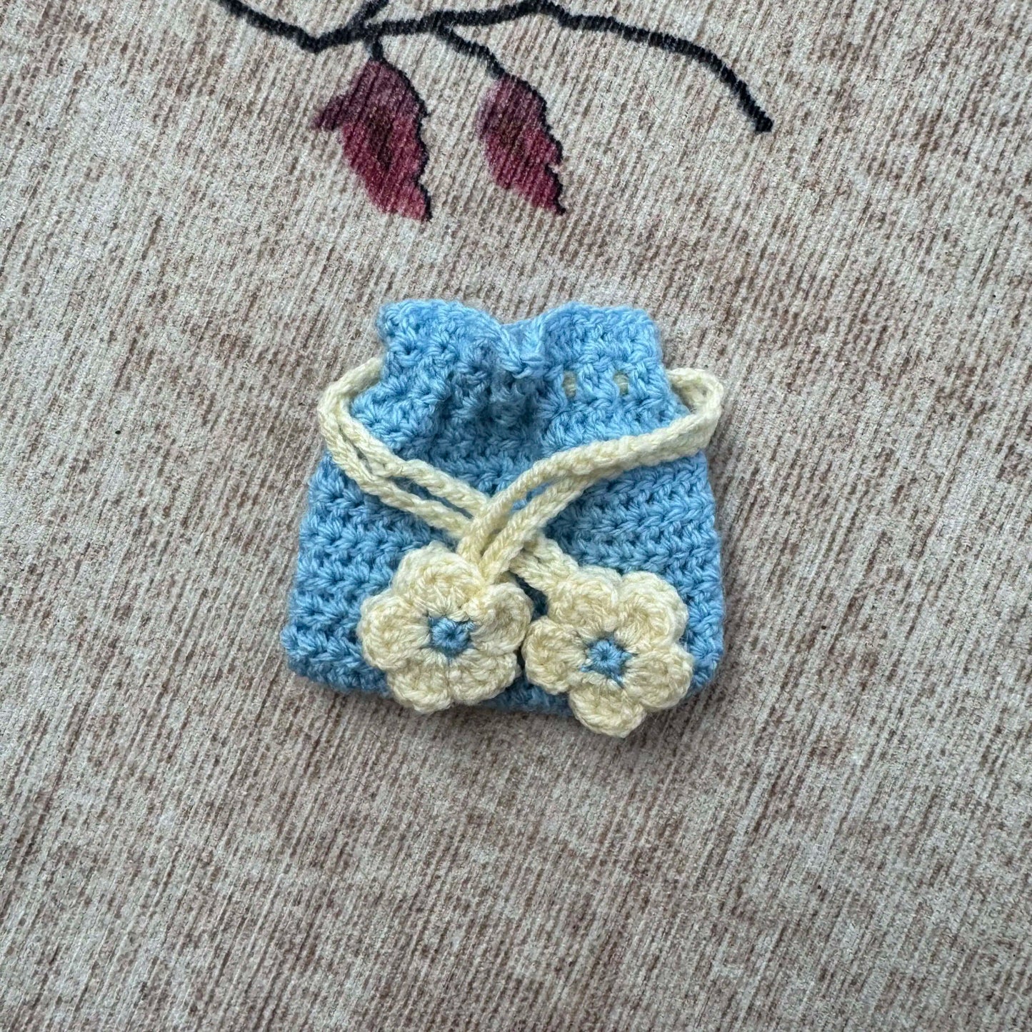 Small blue and cream crocheted bag with flower details on a textured surface.