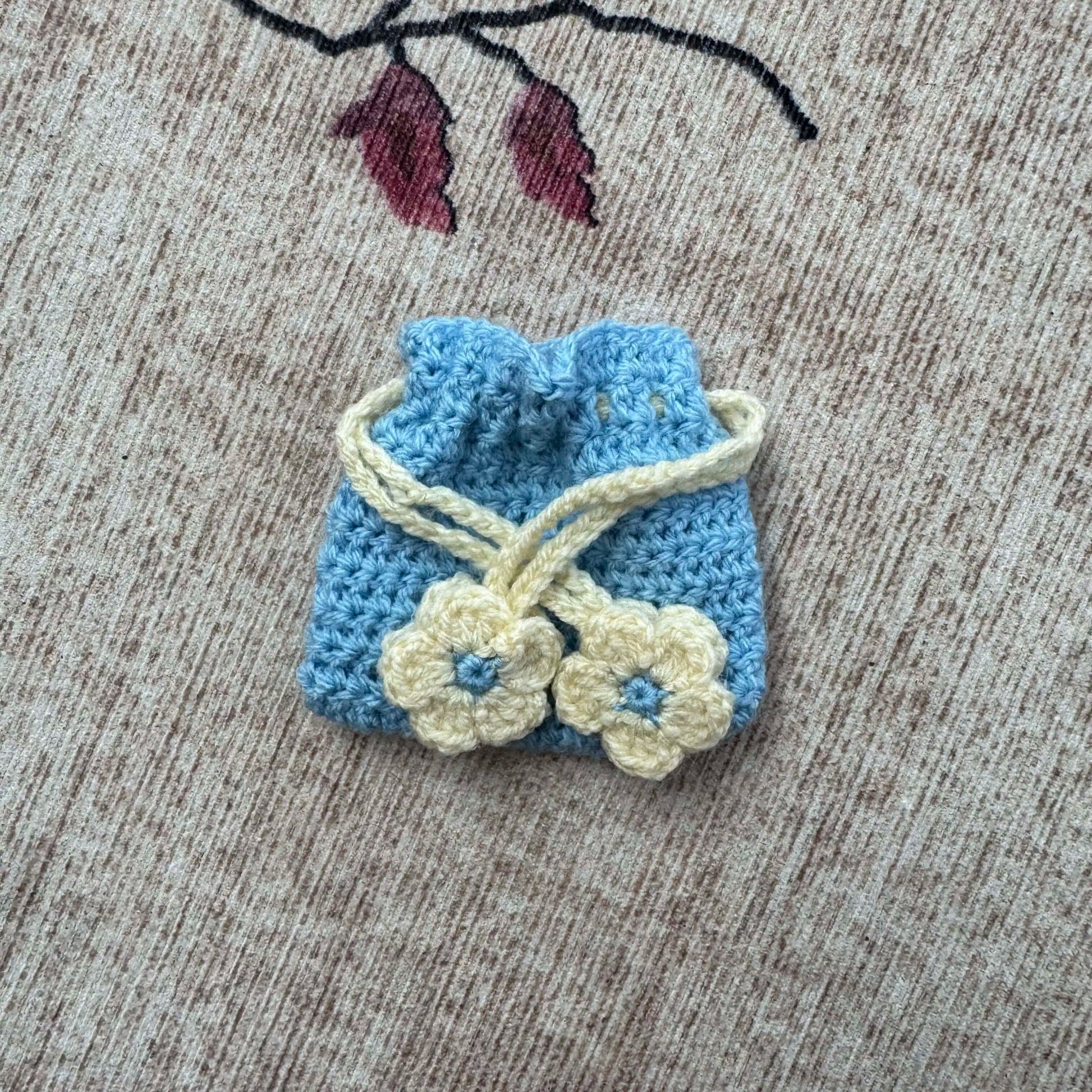 Small blue and cream crocheted bag with flower details on a textured surface.