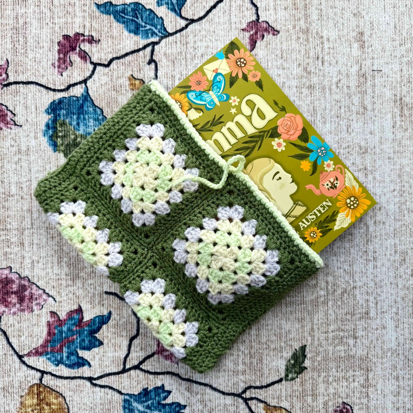 Green crocheted book cover with floral patterns on a floral-patterned fabric background