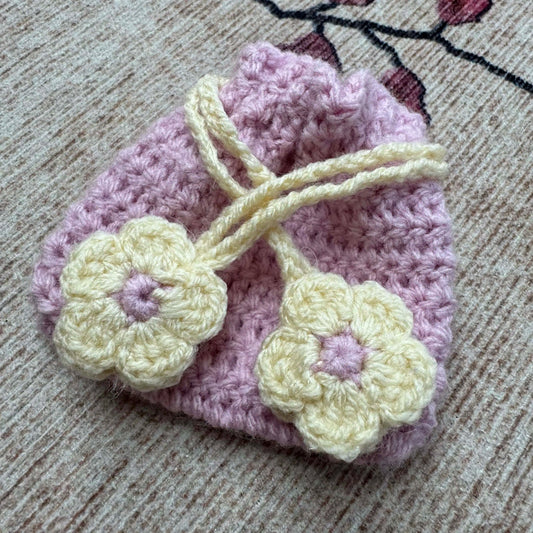 Crocheted pink pouch with yellow flowers on a textured surface