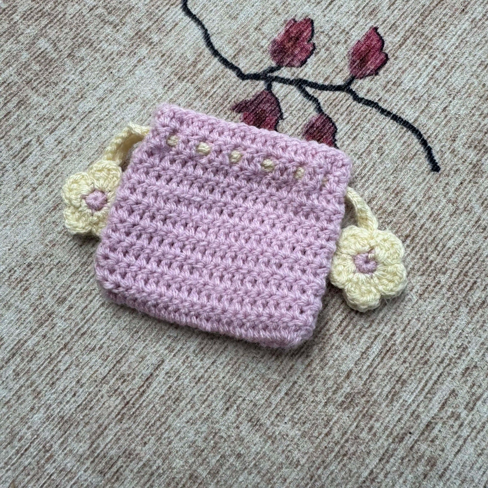 Crocheted lavender pouch with floral decorations on a textured surface