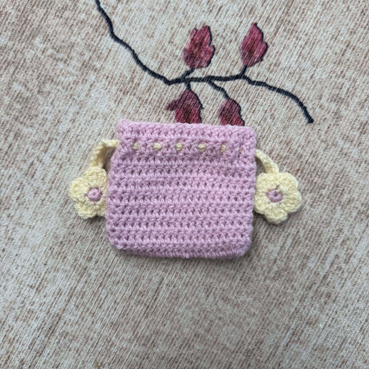 Crocheted pink pouch with floral decorations on a textured surface