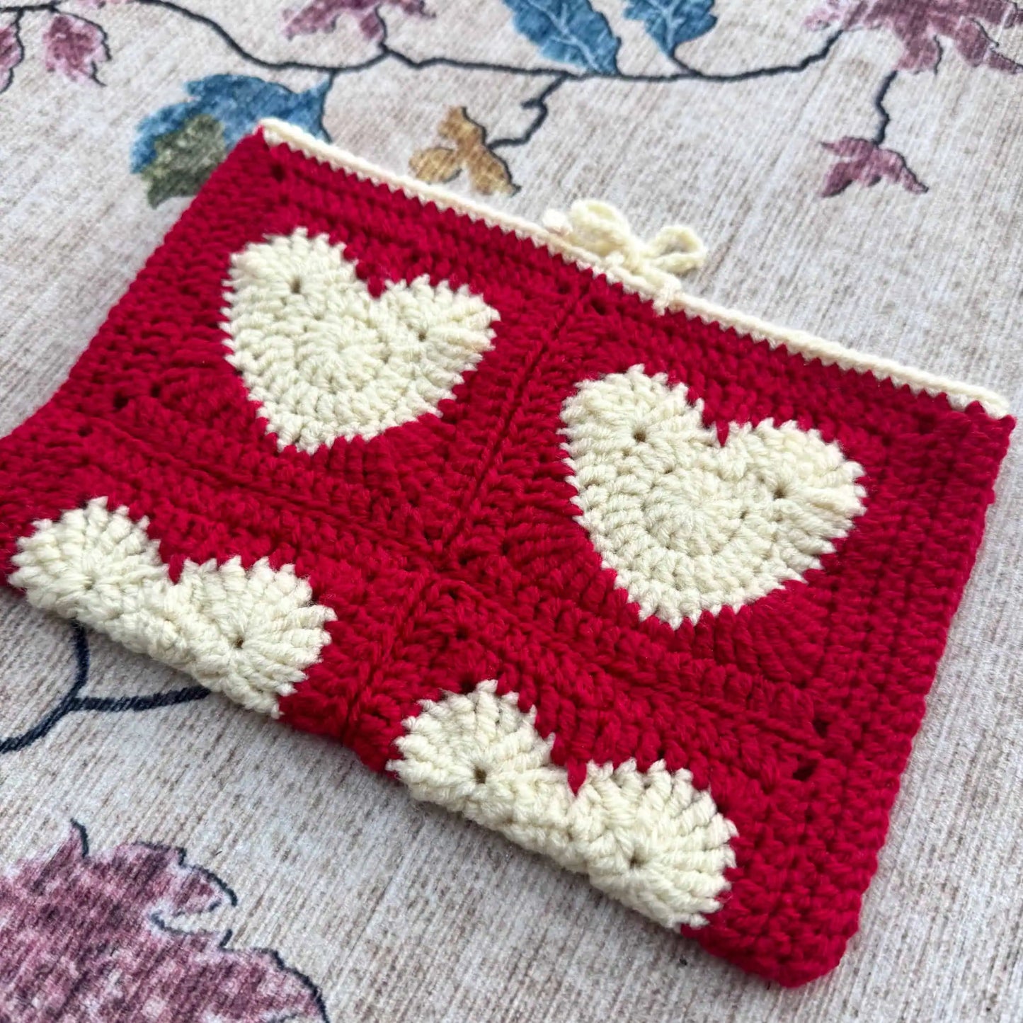 Crocheted book cover with white heart patterns on a floral fabric background