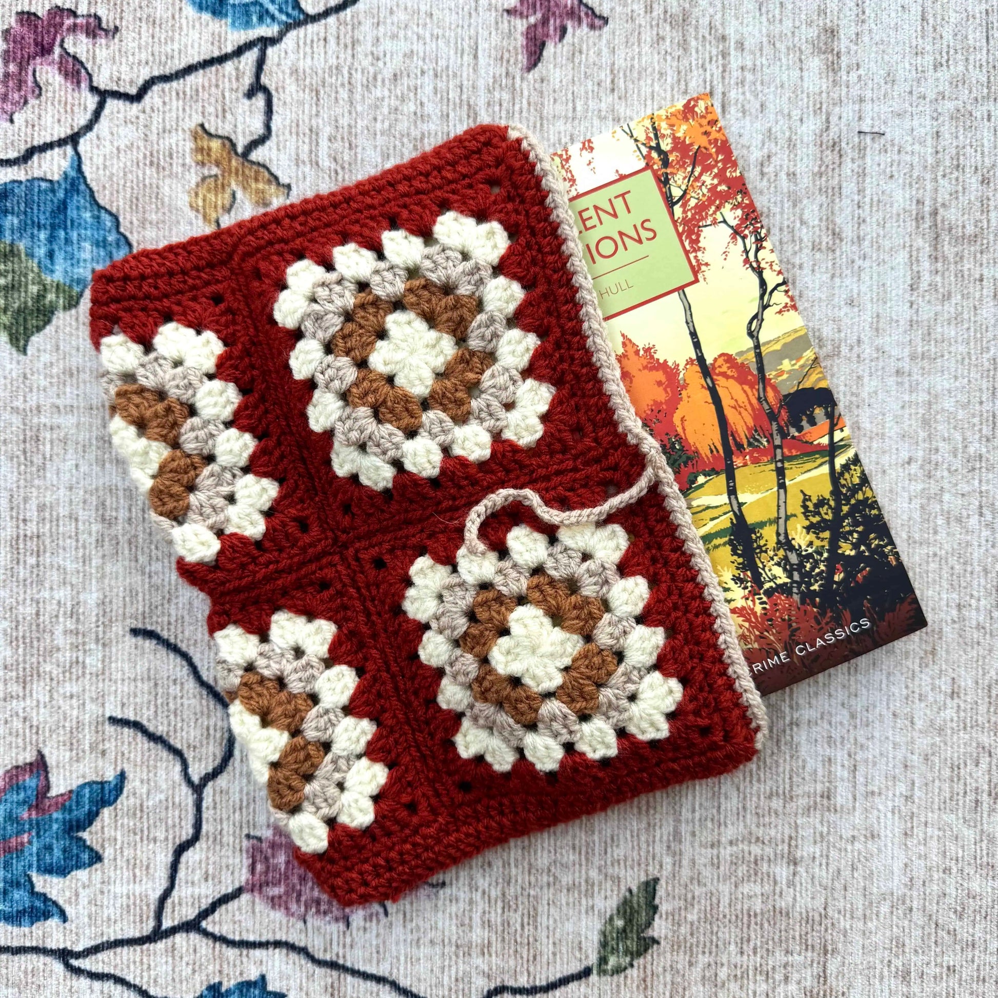 Crocheted book cover with dark red and white patterns on a floral fabric background