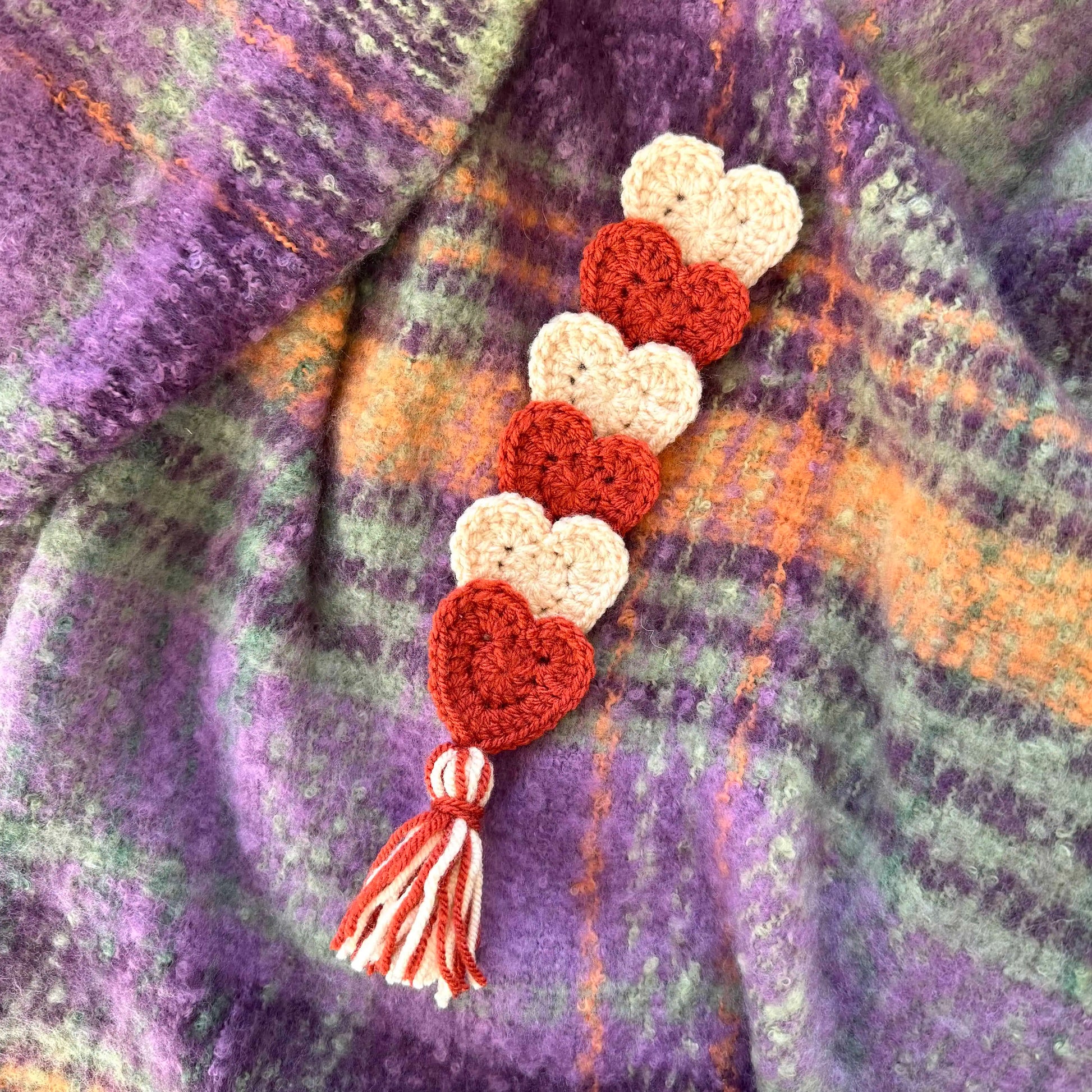 Crocheted heart-shaped bookmark with a tassel on a textured fabric background