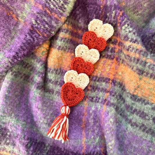 Crocheted heart-shaped bookmark with a tassel on a textured fabric background