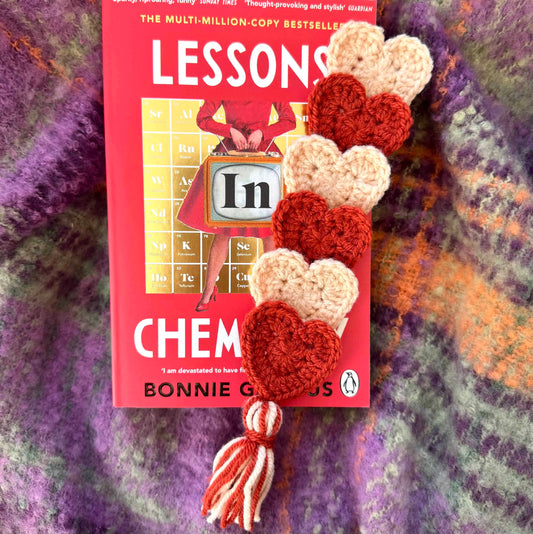 Crocheted heart bookmark on a textured fabric background.